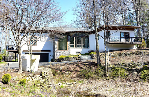 Modern style home with white stucco, hipped roof, stone entry dark window trim.