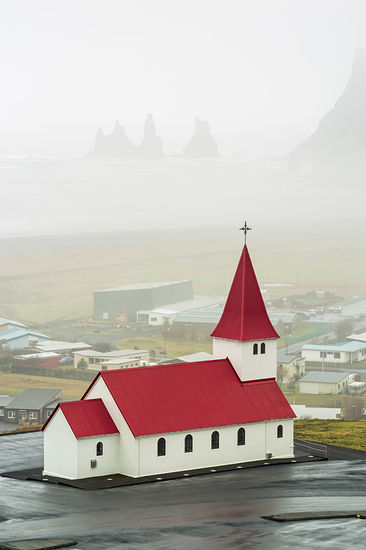Víkurkirkja, also known as the Church of Vík í Mýrdal, is a striking and iconic church located in the village of Vík í Mýrdal, in southern Iceland. Perched on a hill overlooking the picturesque town, this Lutheran church was completed in 1934 and has since become a symbol of the area.
The church is notable for its distinctive architecture, featuring a white exterior with a red roof that stands out against the dramatic backdrop of Iceland's volcanic landscape, including the nearby Reynisfjara black sand beach and the Reynisdrangar sea stacks. The interior of Víkurkirkja is equally charming, with beautiful wooden details and a serene atmosphere.
One of the church's most unique features is its stunning stained glass windows, which depict scenes from Icelandic history and folklore. The church also serves as a community gathering place, hosting various events and services throughout the year.