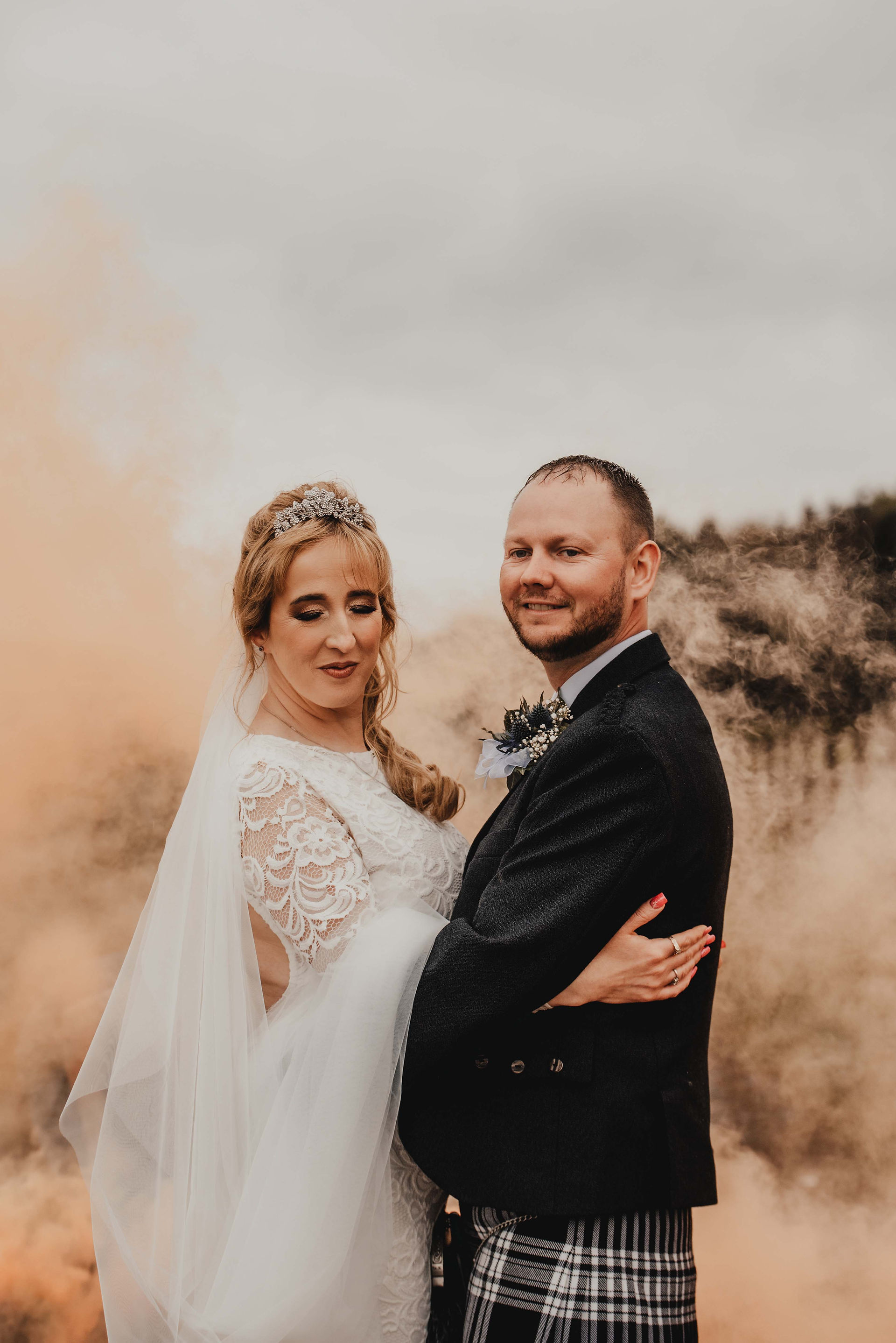 the bride and groom kiss at their wedding in front of a smoke bomb in perthshire