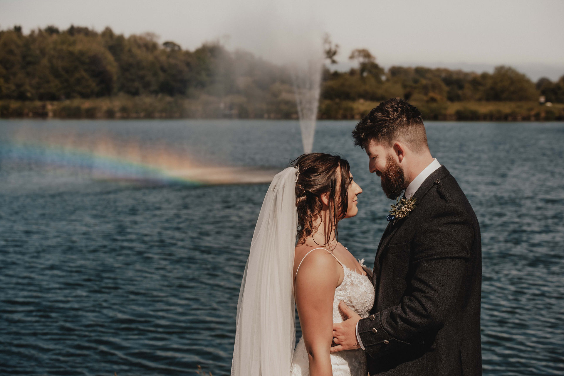 a bride and groom pose in front of the fountain on a sunny day in Dundee. There is a rainbow