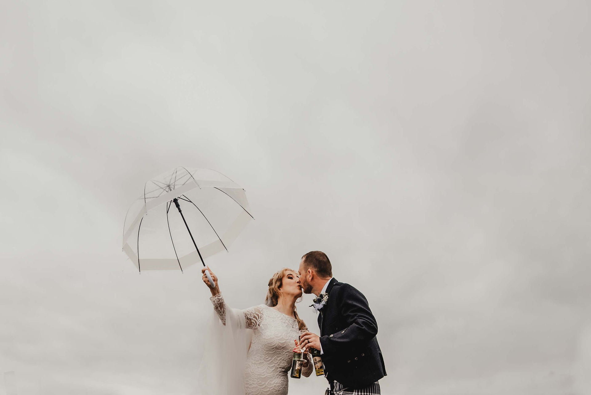 a bride and groom kiss under an umbrella while it rains at their wedding at Bachilton Barn