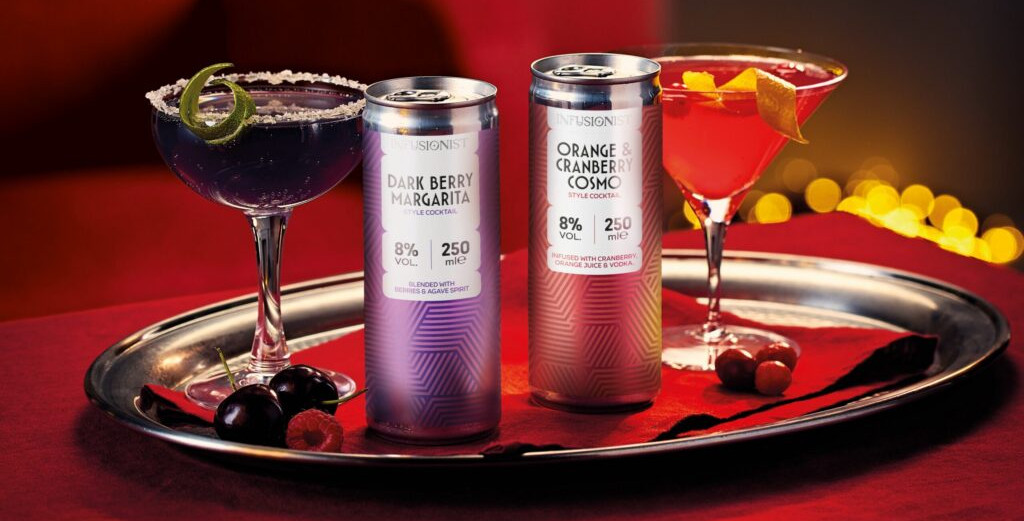 Two cocktail cans and two garnished cocktails on a silver tray, with red lighting and fruit; labels show Dark Berry Margarita and Orange Cranberry Cosmo