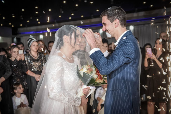 צילום חתונה מלא רגש ושמחה, המתעד את רגע כיסוי ההינומה לפני החופה. החיוכים והקונפטי המשתלבים יחד יוצרים אווירה חגיגית מיוחדת, ומשקפים את ההתרגשות הגדולה של תחילת הטקס