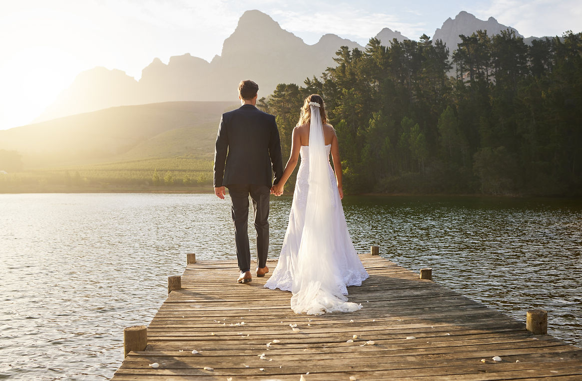 Love, wedding and back of couple by a lake standing, bonding and holding hands on the pier