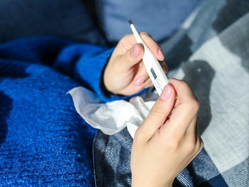 Person laying in bed holding a thermometer and a tissue