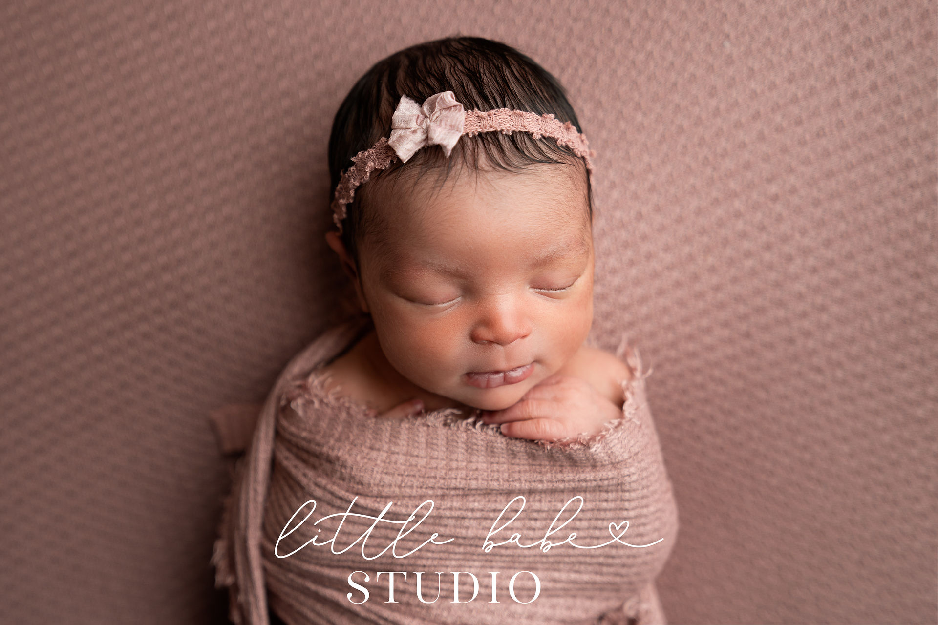 Swaddled baby girl on pink backdrop with matching wrap and headband taken during newborn photos at Little Babe Studio in Middletown, Ohio