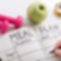 image of someone writing in notebook with words "meal plan." pink weights and green apple in image.