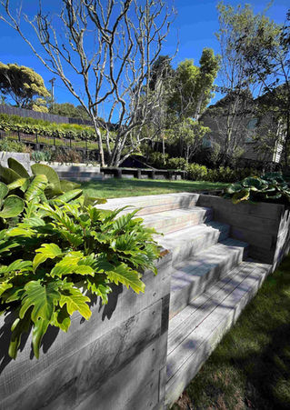 Weathered timber sleeper steps built into a sloping lawn section next to a structural timber planter box in Raglan by Virginia Watt.