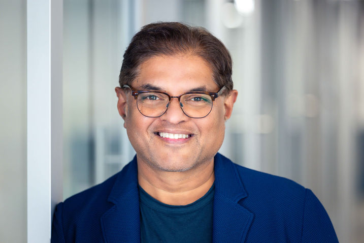 Man in a blue blazer smiling warmly in front of blurred glass office panels
