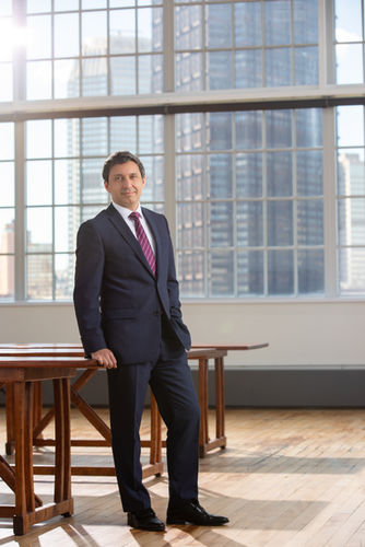 Man in a business suit standing near floor-to-ceiling windows in a corporate office
