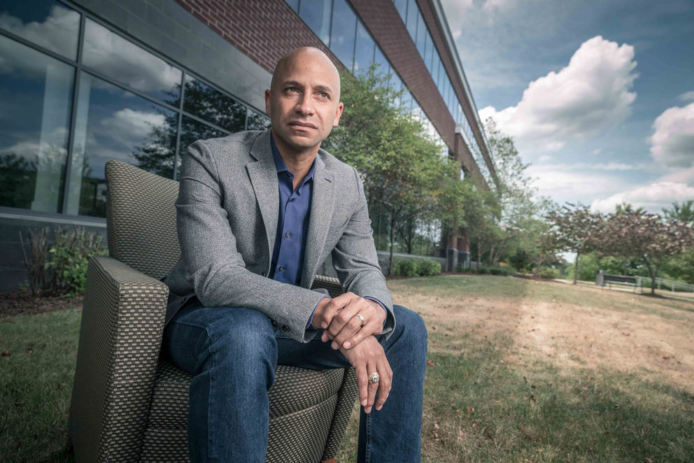 Businessman sitting on an outdoor bench, with a grassy field and office buildings behind him