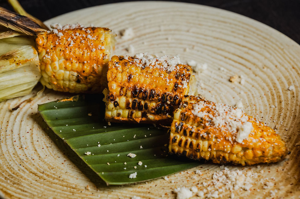 Street Elote, fire-grilled sweet corn coated in cotija cheese, lime crema, and smoky chipotle aioli, finished with tajín seas