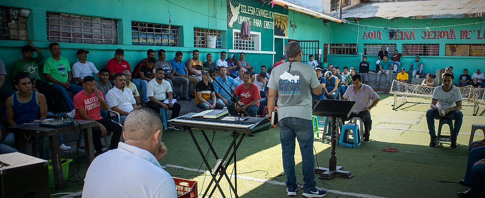 Pastor stands in rundown building with prisoners holding care packages
