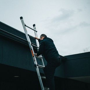 Person climbing an extension ladder during an outdoor installation