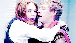 Amy and Rory mouths open embracing. Amy in police uniform, Rory as a roman