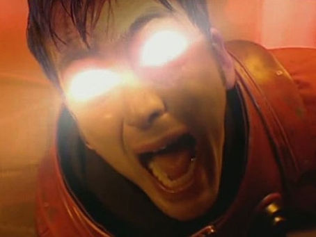 The Doctor in orange spacesuit screaming as light shines brightly from his eyes