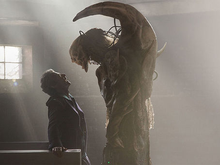 The Fisher King towering over the Doctor. Both are looking at each other, the Fisher King is like a skull face with wings, but they aren't wings, more like bone. Apologies, this is a rubbish description.