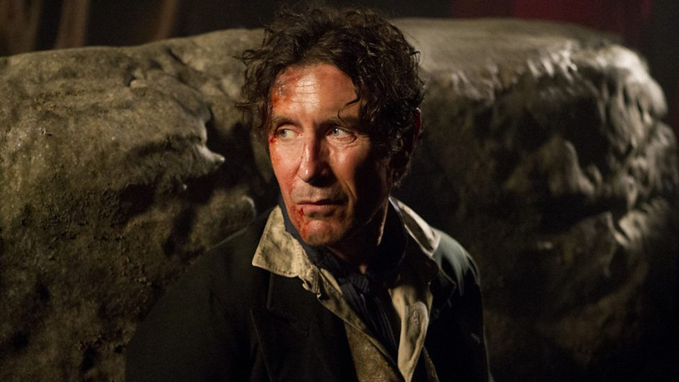 Eighth Doctor against a rock, his face is bloody