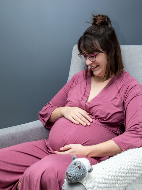 Pregnant woman in red rose housecoat looking down at her beautiful belly