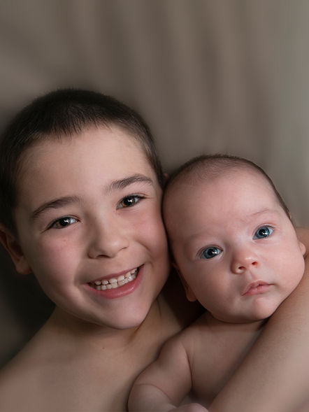 Newborn baby with older sibling on neutral background