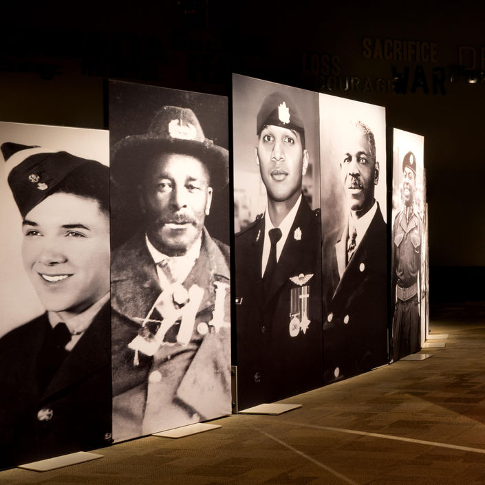Large black-and-white portrait panels of Black Canadian military service members forming a curved exhibition pathway.
