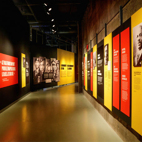 Dark museum corridor showcasing an exhibit of large portraits and bright yellow and red panels showcasing Black military history in Canada.