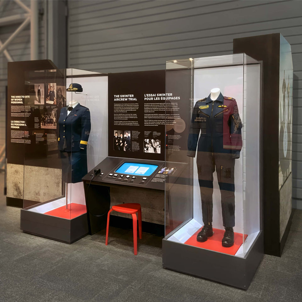 Large red and black exhibition section, featuring various image and text layouts, and two display cases containing RCAF uniforms.
