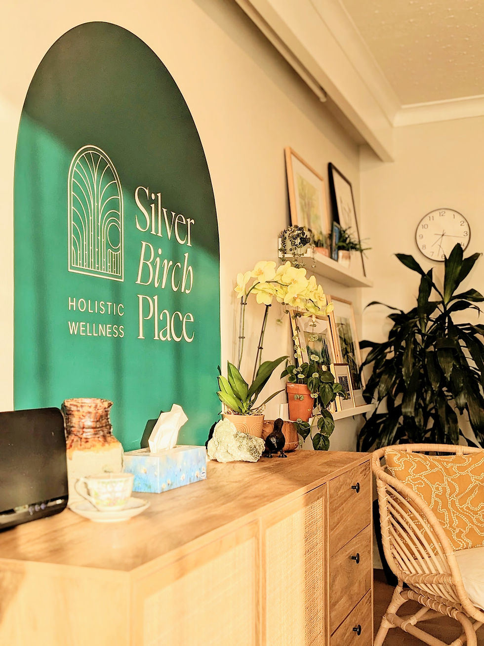 A wooden sideboard decorated with pottery, crystals, and potted plants sits beneath a large green arched wall feature displaying the Silver Birch Place Holistic Wellness logo.
