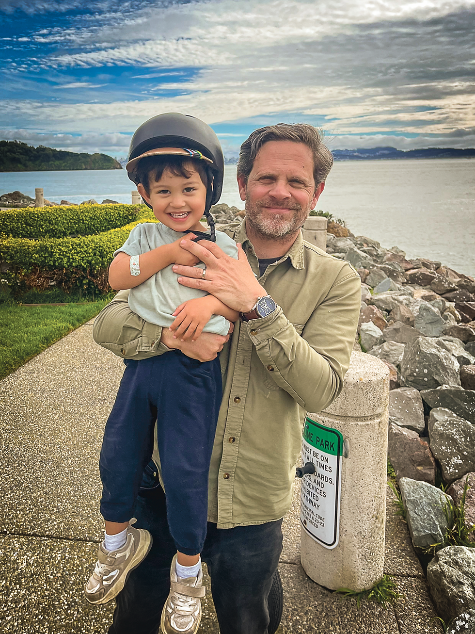 Justin Girardi holds his son Enzo, 3, along the Shoreline Park seawall in Tiburon on Feb. 25. The father-son duo regularly ride the park’s waterfront path, with Enzo on his Strider balance bike, before hunting for crabs at the rocky cove below. (Tyler Callister / The Ark)