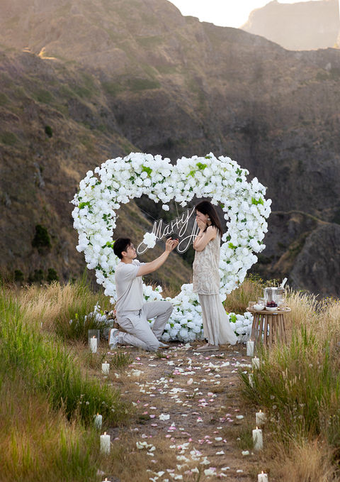 Man proposing on one knee beneath a white floral heart in Madeira