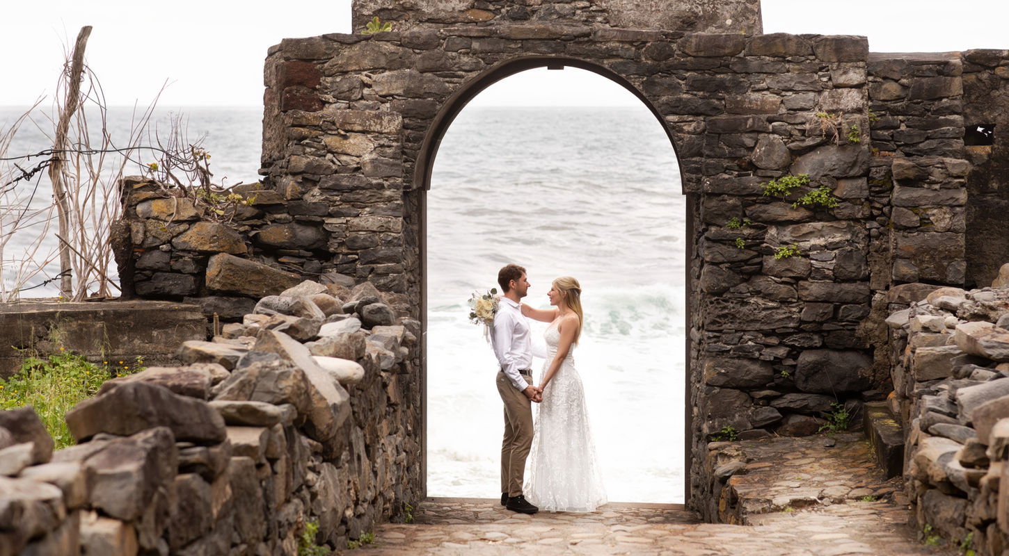 Elopement couple standing beneath a historic seaside arch in Madeira during an intimate wedding photoshoot.