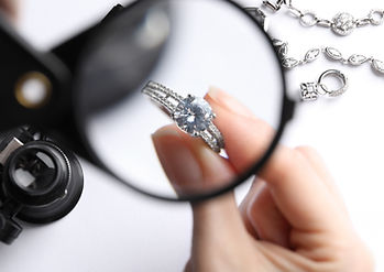 Jeweler examining diamond ring with magnifying glass at white table, closeup.jpg
