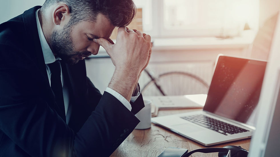 Man in suit sits at desk with head in hands, laptop open. Stuck in his Job Search
