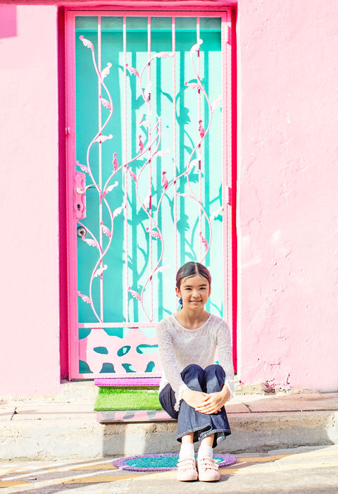 Young child sitting on steps in front of a vibrant pink and turquoise door in Haji Lane, Singapore, during a colorful and artistic children's portrait session