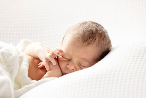 Newborn baby sleeping peacefully on a soft white blanket in a natural light studio photography session in Singapore