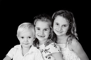 Three smiling siblings posing together in a black and white studio family photography session
