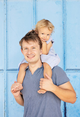 Father carrying his young child on his shoulders in front of a vibrant blue wooden door in Joo Chiat, Singapore, during a candid family photography session
