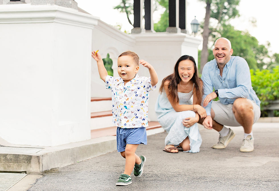 Young child running happily towards the camera while his parents laugh behind him at the Singapore Botanic Gardens