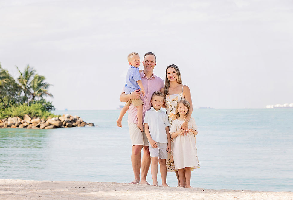 Family of five standing together on Sentosa Beach with calm sea and tropical greenery behind them