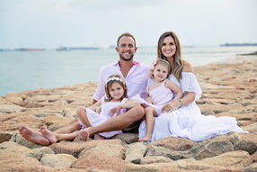 Family sitting together on a rocky beach, dressed in soft pastel tones, during a serene coastal family photography session
