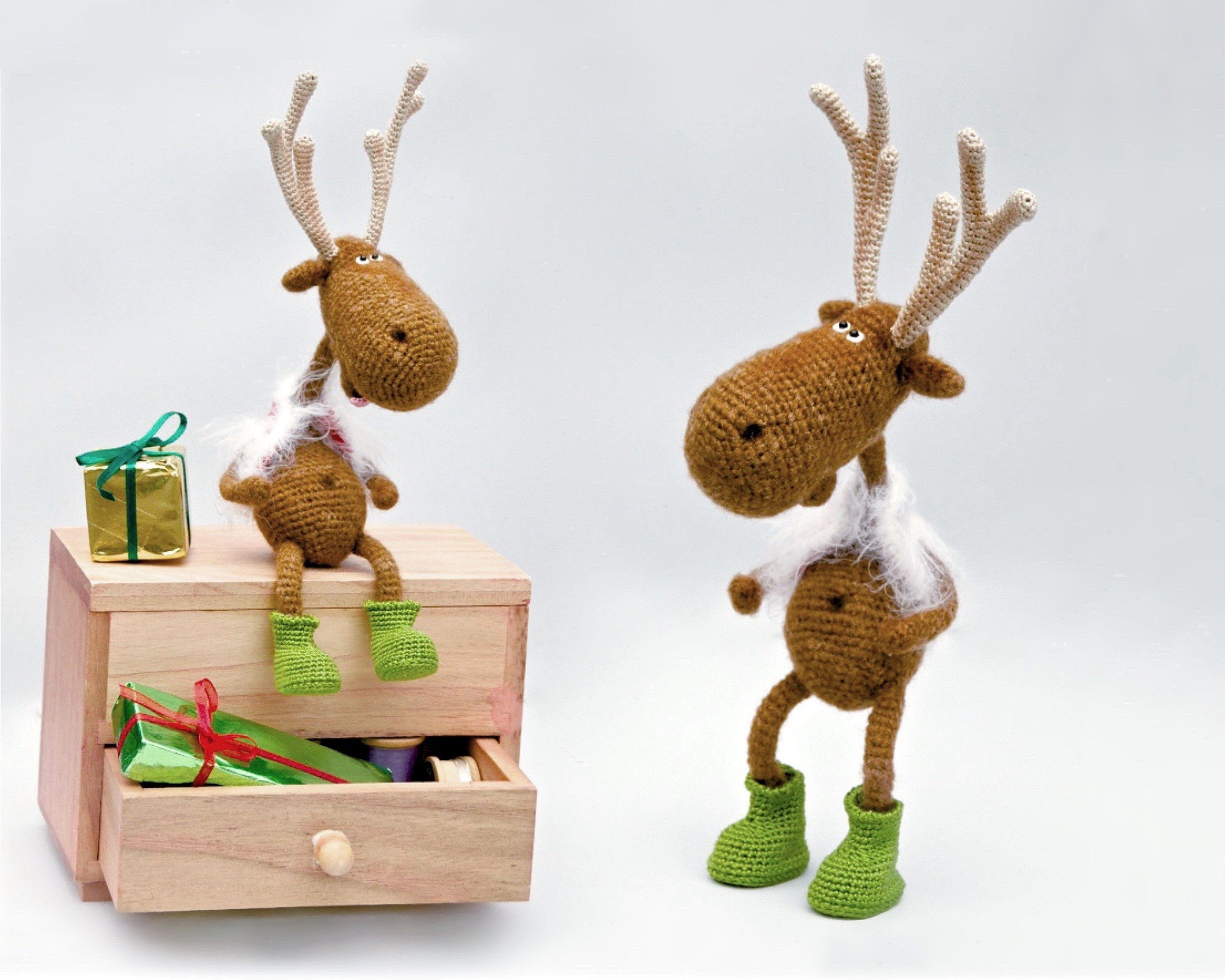 Crochet reindeer in red vest and green boots sitting on a wooden chest