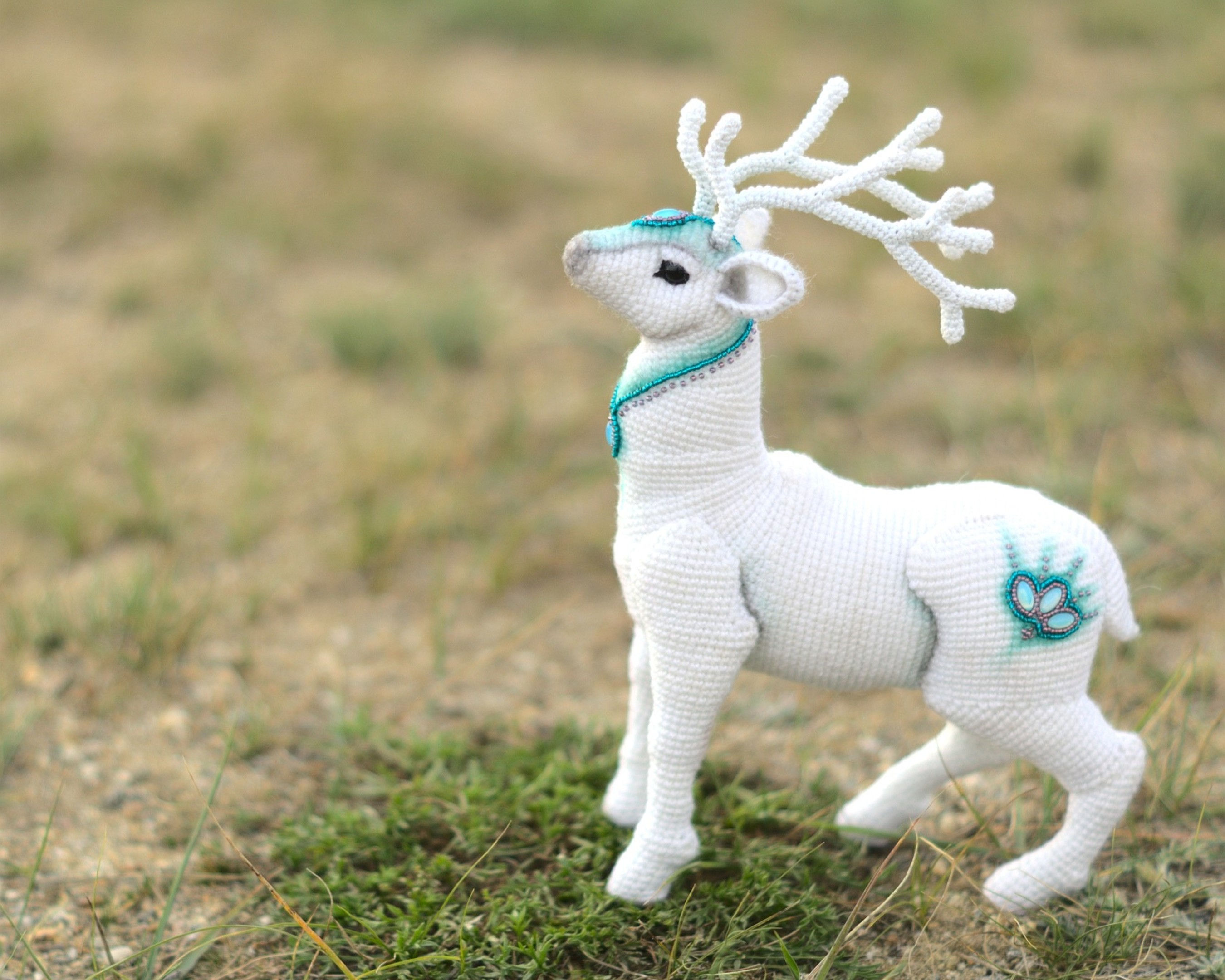 Crochet white Patronus stag with turquoise ornaments on the grass
