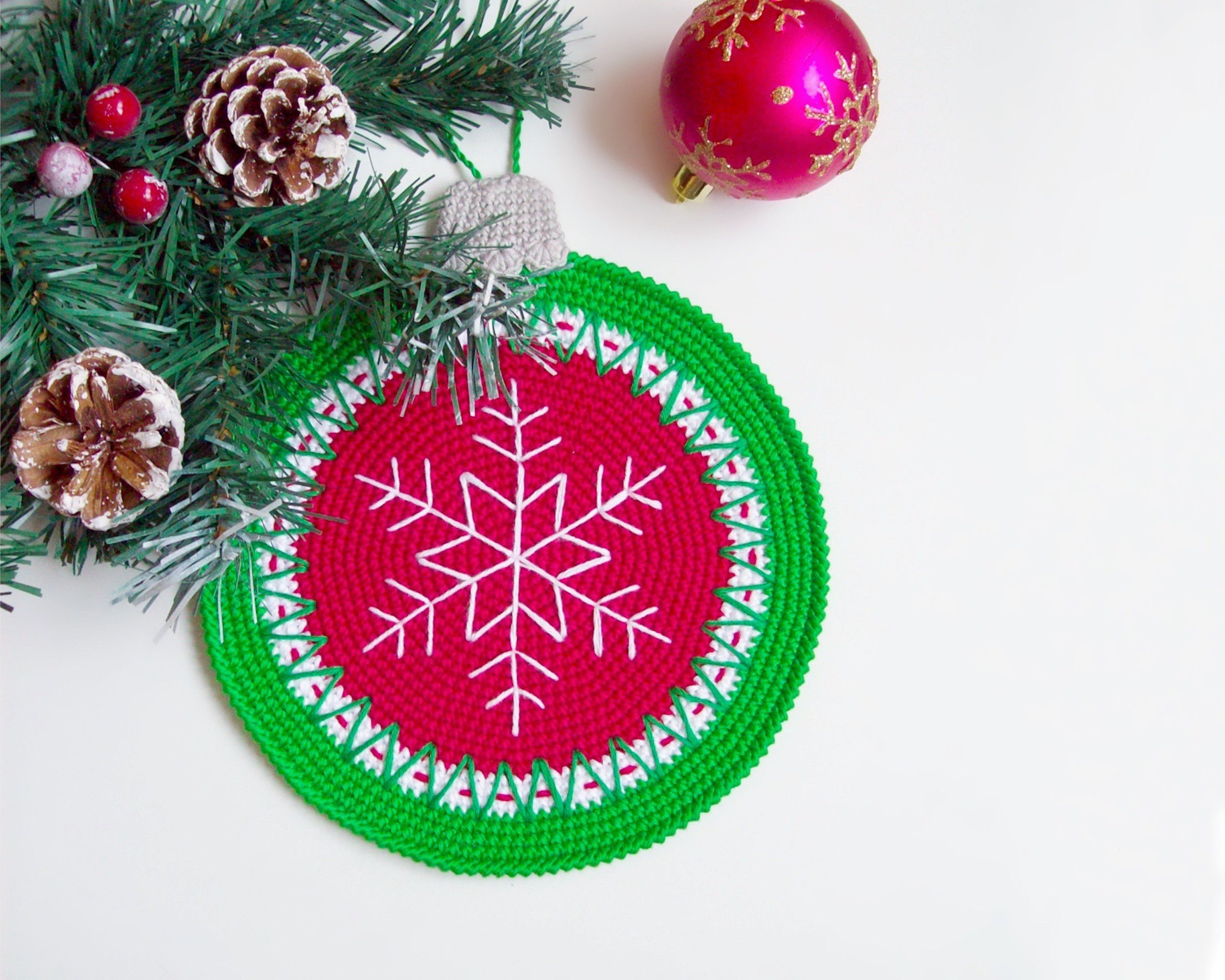 Drei gehäkelte Weihnachtskugel Topflappen mit Schneeflocken unter Tannenzweigen