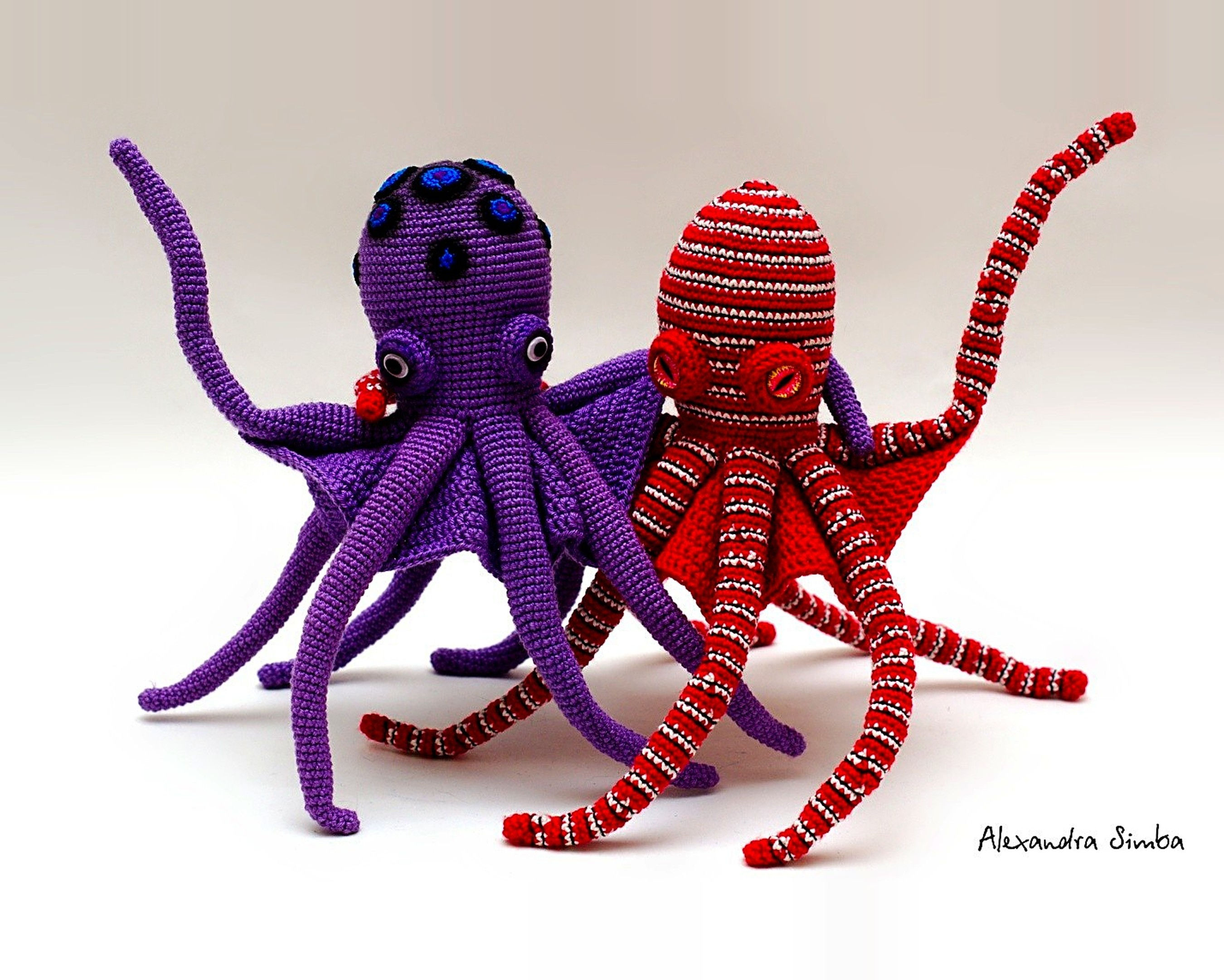 Two crochet mimic octopuses in purple and red-and-white stripes