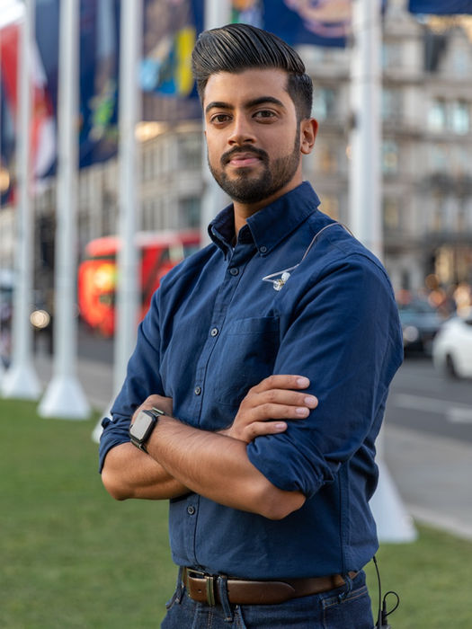 Man in blue shirt standing with arms crossed outdoors.