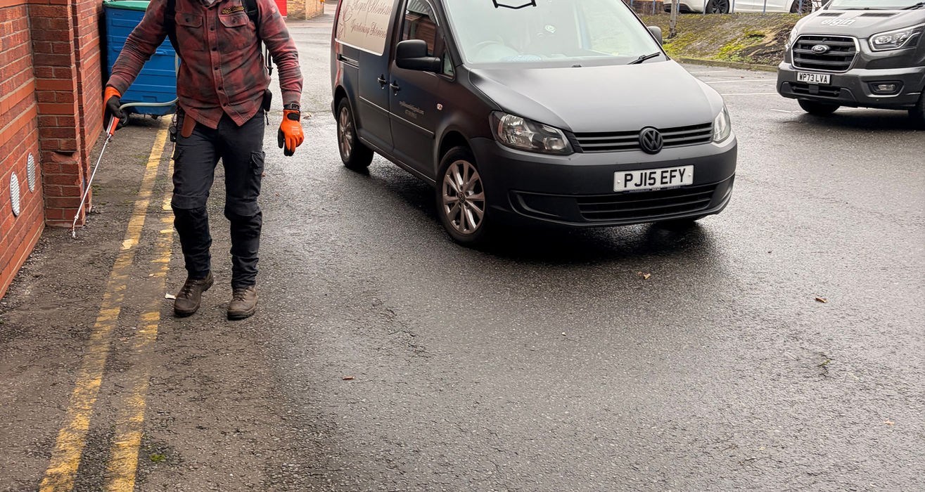 Man spraying wall near black van FJ18 BPY in industrial area.