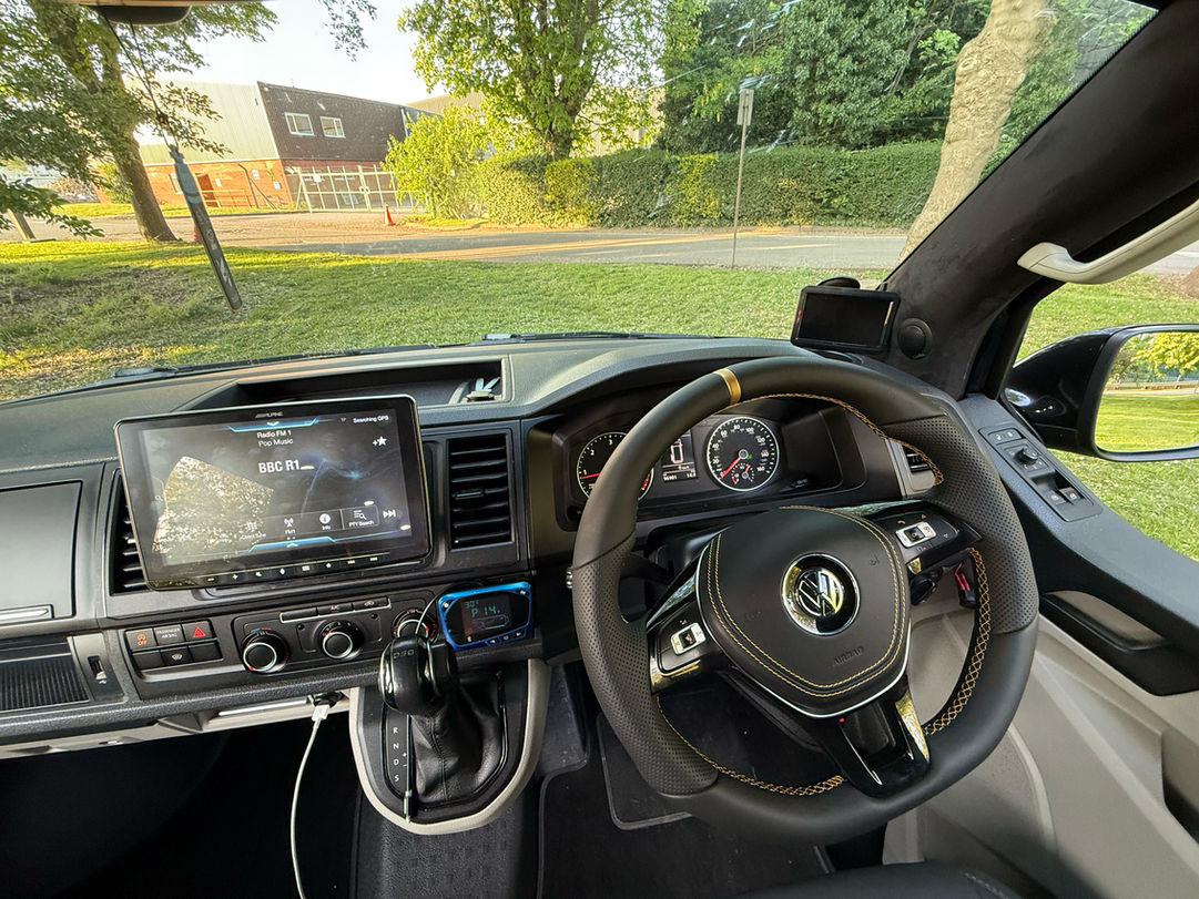 VW campervan interior: black leather steering wheel, infotainment screen showing 88C R1, modern dashboard