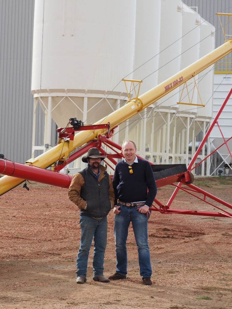 Two men standing in front of large white storage silos.