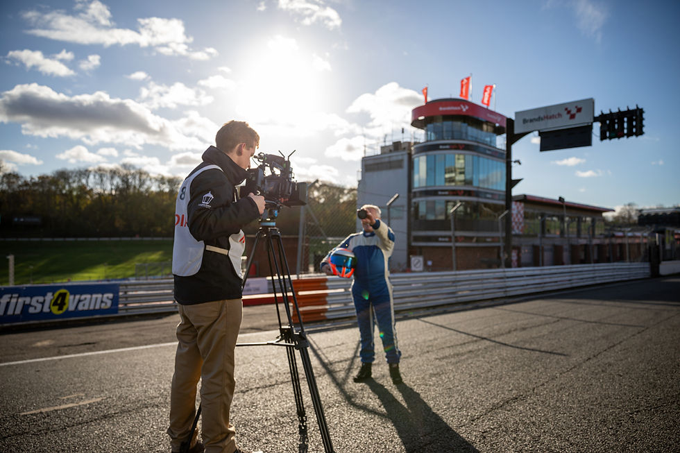 Cameraman filming a racing driver on a track at sunset.