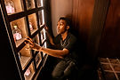 Young Black man examining a shelf of bottles inside a dimly lit room.